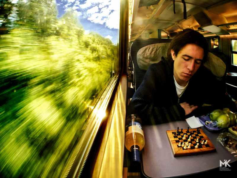 Sitting by the train window and looking at a chess game while traveling trough green woods. 