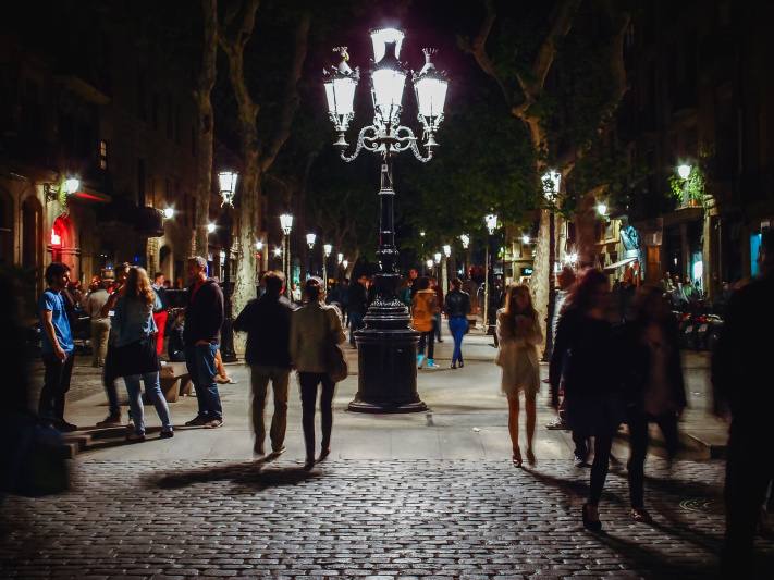 Barcelona, curlicue street lamp, narrow tree alley, pedestriants passing, romantic night walk